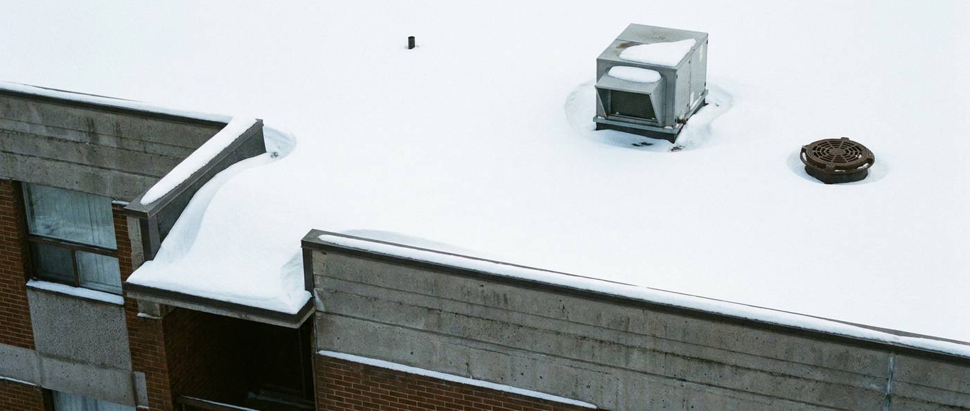 Snow-covered flat commercial rooftop with parapet walls and roof drains
