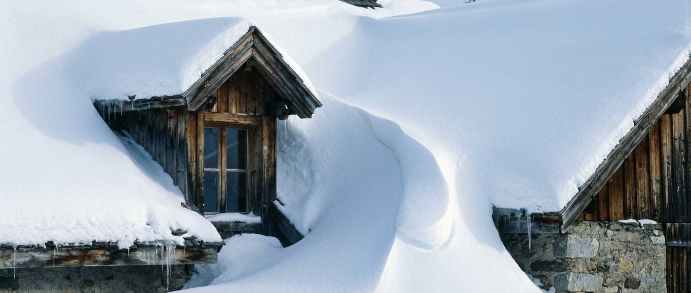 Wind-drifted snow piled deeply against a dormer and roof valley