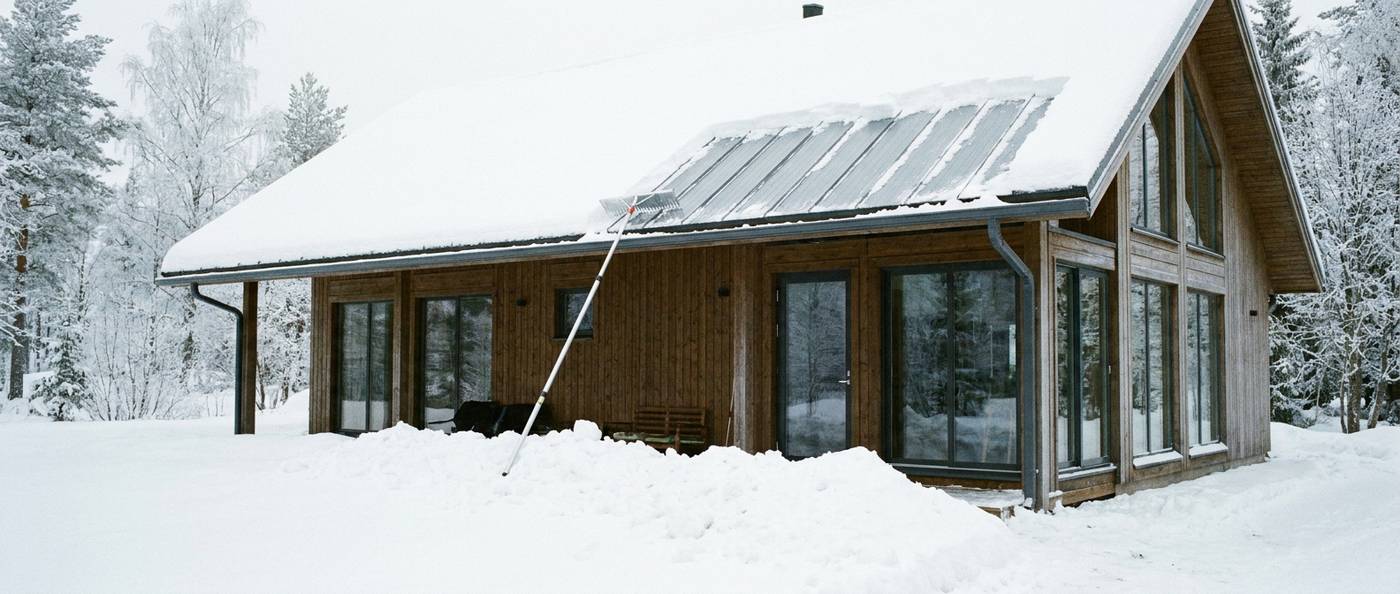 Long-handled roof rake pulling snow down from the edge of a roof