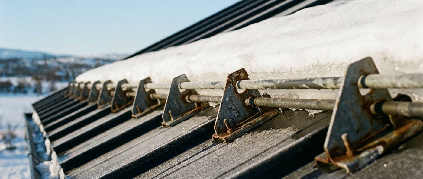 Row of snow guards clamped to a standing-seam metal roof holding snow in place