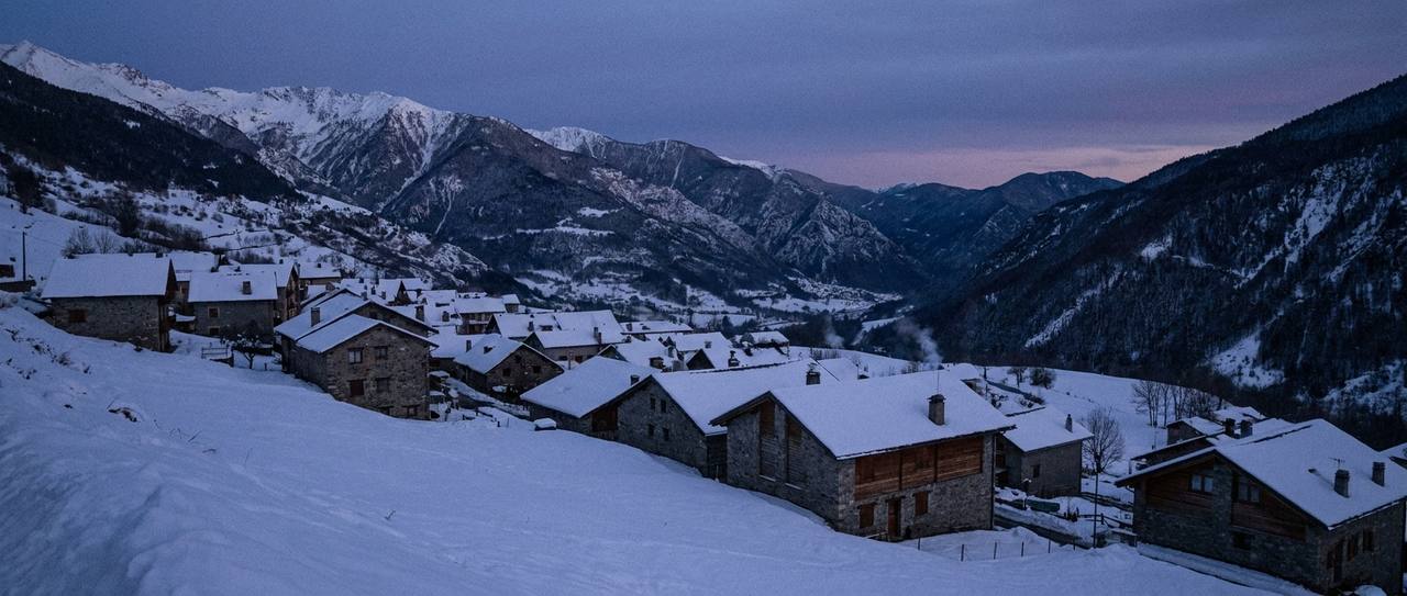 Snow-covered residential rooftops across a mountain valley town at dusk