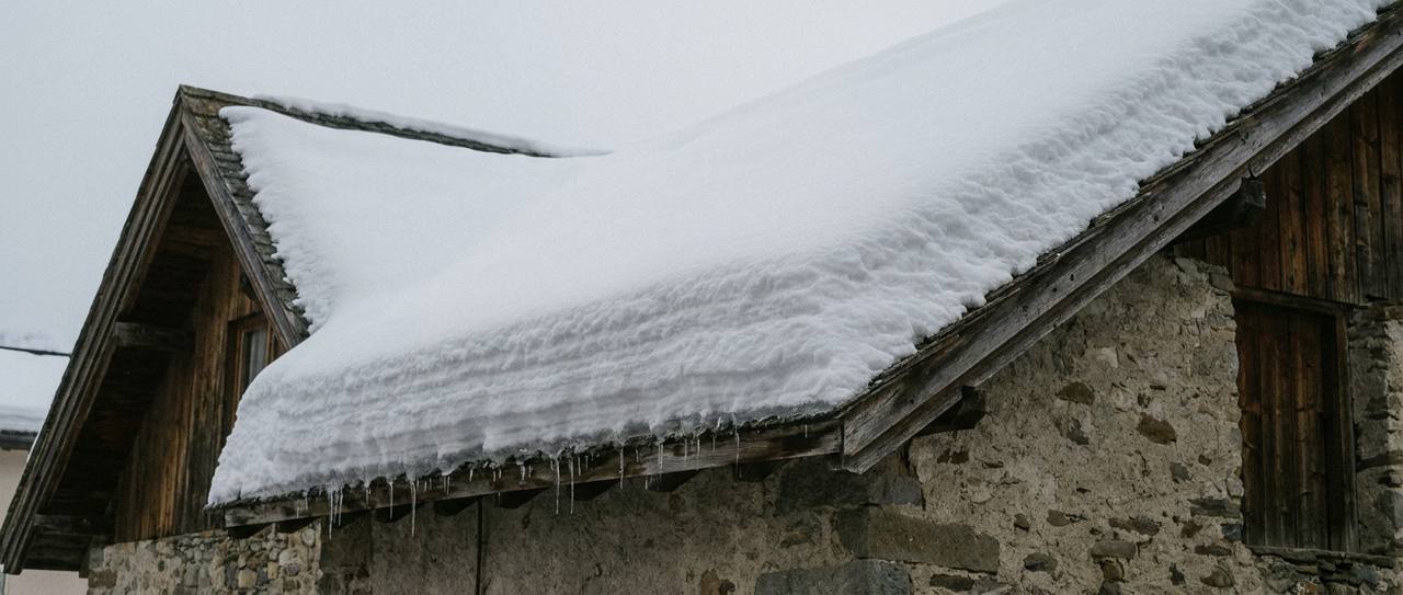 Deep settled snowpack on a residential roof with icicles hanging at the eave